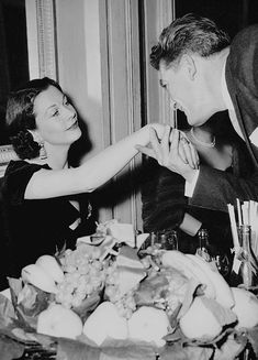 a man and woman sitting at a table with food in front of them, one holding the other's hand