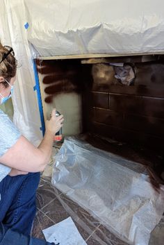 a woman is painting a fireplace with brown paint on the wall and white sheeting