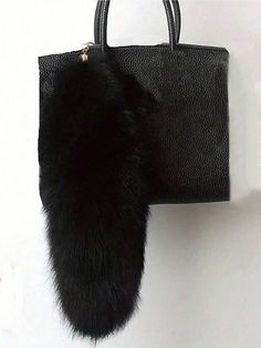 a black bag hanging on the wall with a fur ball attached to it's handle