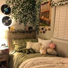 a bed with pillows and stuffed animals on it in a room decorated with green plants