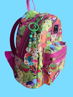 the back side of a colorful backpack with cartoon characters and beads on it, against a blue background