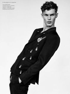 a young man is posing for the camera in a black shirt and pants with an embellishment on his jacket