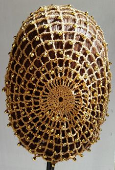 a gold beaded ball on a stand with a white wall in the back ground