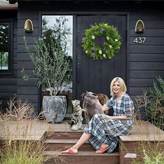 a woman sitting on steps with her dog and cat in front of a house that is decorated with wreaths