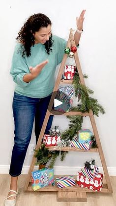 a woman standing in front of a christmas tree with presents on the bottom shelf and pointing at it