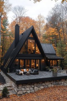 a large black cabin in the woods with lots of trees and leaves on the ground