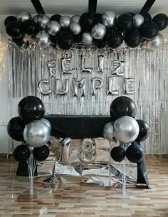 black and silver balloons are hanging from the ceiling in front of a table with a black cloth on it