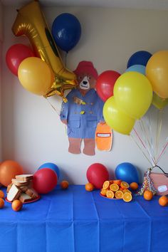 a table topped with balloons and oranges next to a teddy bear