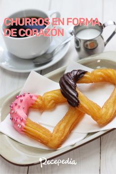 two heart shaped donuts with chocolate frosting and sprinkles on a plate next to a cup of coffee