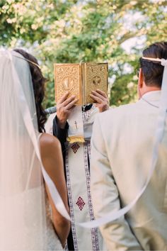 a bride and groom holding up a golden book during their wedding ceremony at the park