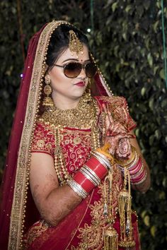 a woman in a red and gold bridal outfit with sunglasses on her head holding a small item