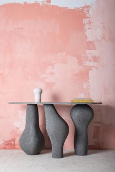 two gray vases sitting next to each other on a table in front of a pink wall