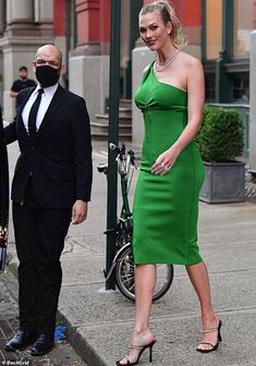 a woman in a green dress is walking down the street next to a man wearing a mask