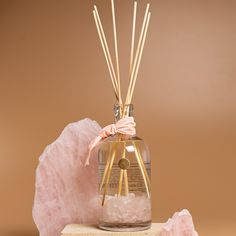 a glass bottle with reeds in it next to pink crystals