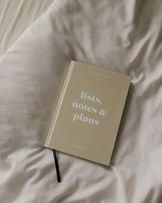 an open book sitting on top of a bed next to white sheets with writing that reads lists, notes & plans