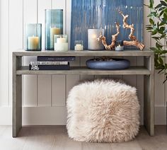 a table with candles, books and a sheepskin ottoman in front of it on the floor