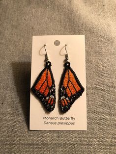 a pair of orange and black earrings with monarch butterfly wings hanging from it's earwires