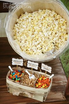 a table topped with lots of different types of candy and candies next to a big bowl of popcorn