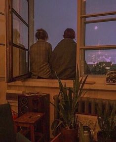 two people are sitting on a window sill looking out at the city below them