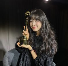 a woman holding an award in front of a dark background with light from the spotlight