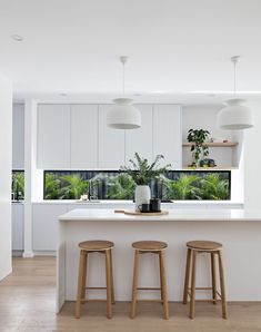 two stools in front of an island with plants on it and lights hanging from the ceiling