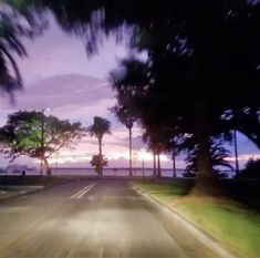 the sun is setting behind palm trees on the side of the road with no cars