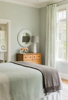 a bedroom with light green walls and white bedding, an oval mirror on the wall