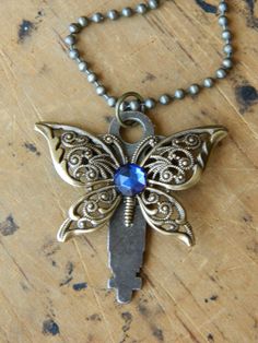 a necklace with a butterfly on it and a blue crystal stone in the center is sitting on a wooden surface