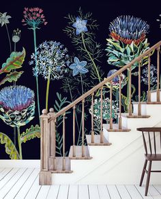 a stair case with flowers painted on the wall next to a wooden table and chair