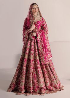 a woman in a pink and gold wedding dress standing next to a white wall with her hands on her chest