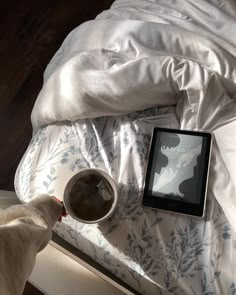 a cat standing next to a tablet on a bed