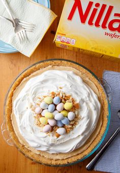 a pie with white frosting and candy on top next to a box of nilla wafers