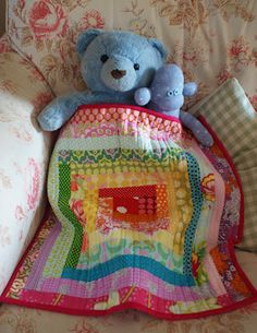 a blue teddy bear sitting on top of a couch next to a colorful blanket and pillow