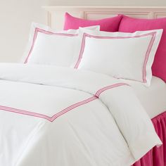 a bed with white sheets and pink pillows