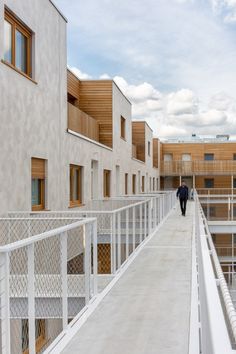 two people walking down a walkway between two buildings with balconies on each side