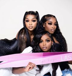 three women are posing for the camera with one holding a pink ribbon in front of them