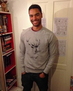 a man standing in front of a book shelf wearing a sweater with an image of a deer on it