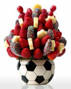 a vase filled with lots of fruit sitting on top of a soccer ball covered in sprinkles