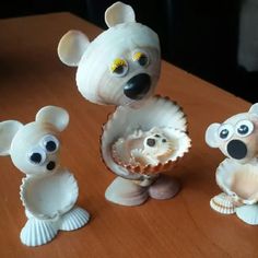 three small figurines sitting on top of a table next to an open seashell