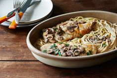 a bowl filled with pasta and mushrooms on top of a wooden table next to silverware