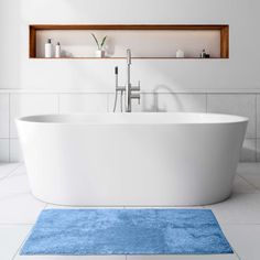 a white bath tub sitting on top of a bathroom floor next to a blue rug