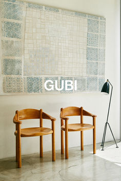 two wooden chairs sitting next to each other in front of a wall with the word gubi on it