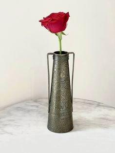 a single rose in a metal vase on a marble table