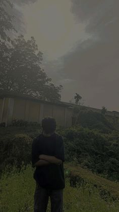 a man standing in the grass with his arms crossed looking up at an overcast sky