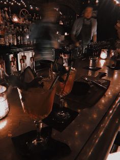 two cocktails sitting on top of a bar next to bottles and glasses filled with liquid