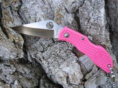 a pink pocket knife on a chain hanging from a tree trunk with rocks in the background