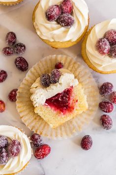 cupcakes with white frosting and raspberry toppings on a marble surface