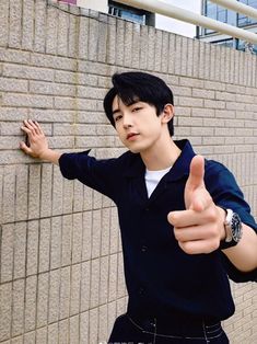 a young man standing next to a brick wall giving the thumbs up sign with his hand