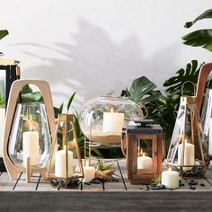 several different types of candles are sitting on a table with plants and mirrors behind them