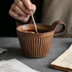 a person is spooning something into a bowl on a table with an open book